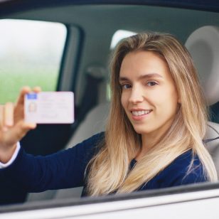 A young woman holds up her driver's license in a car